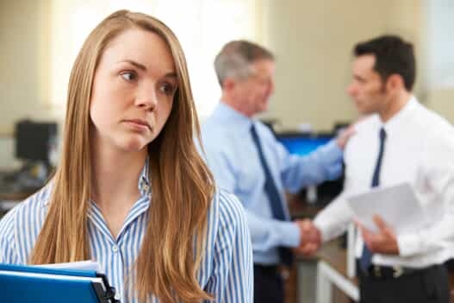 A woman seems upset by two men having a conversation behind her in an office setting